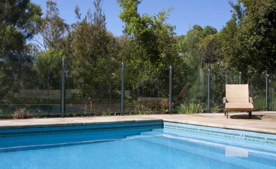 Clear Pool With Glass Fence And Trees In The Background